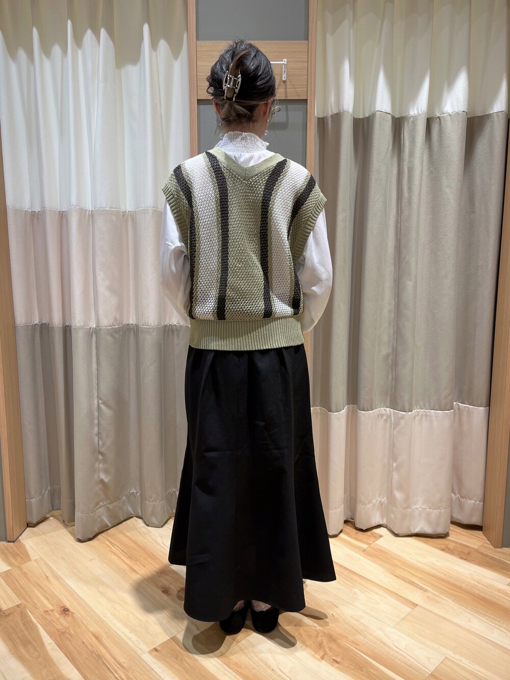 グリーン系のベスト、ブラック系のスカートを着用したレディースの春コーディネートの3枚目の写真