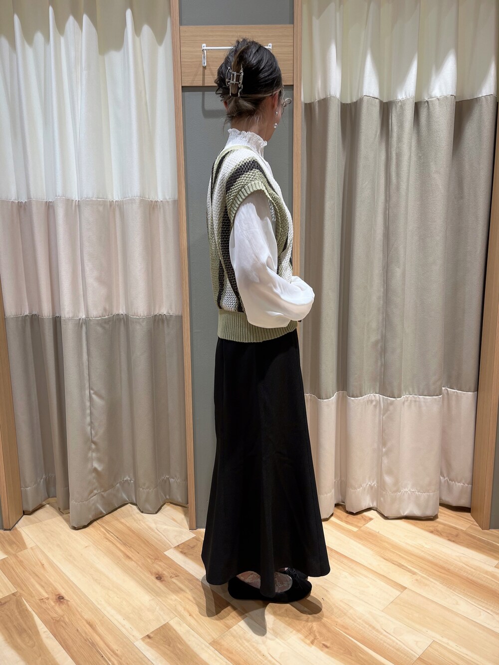 グリーン系のベスト、ブラック系のスカートを着用したレディースの春コーディネートの2枚目の写真