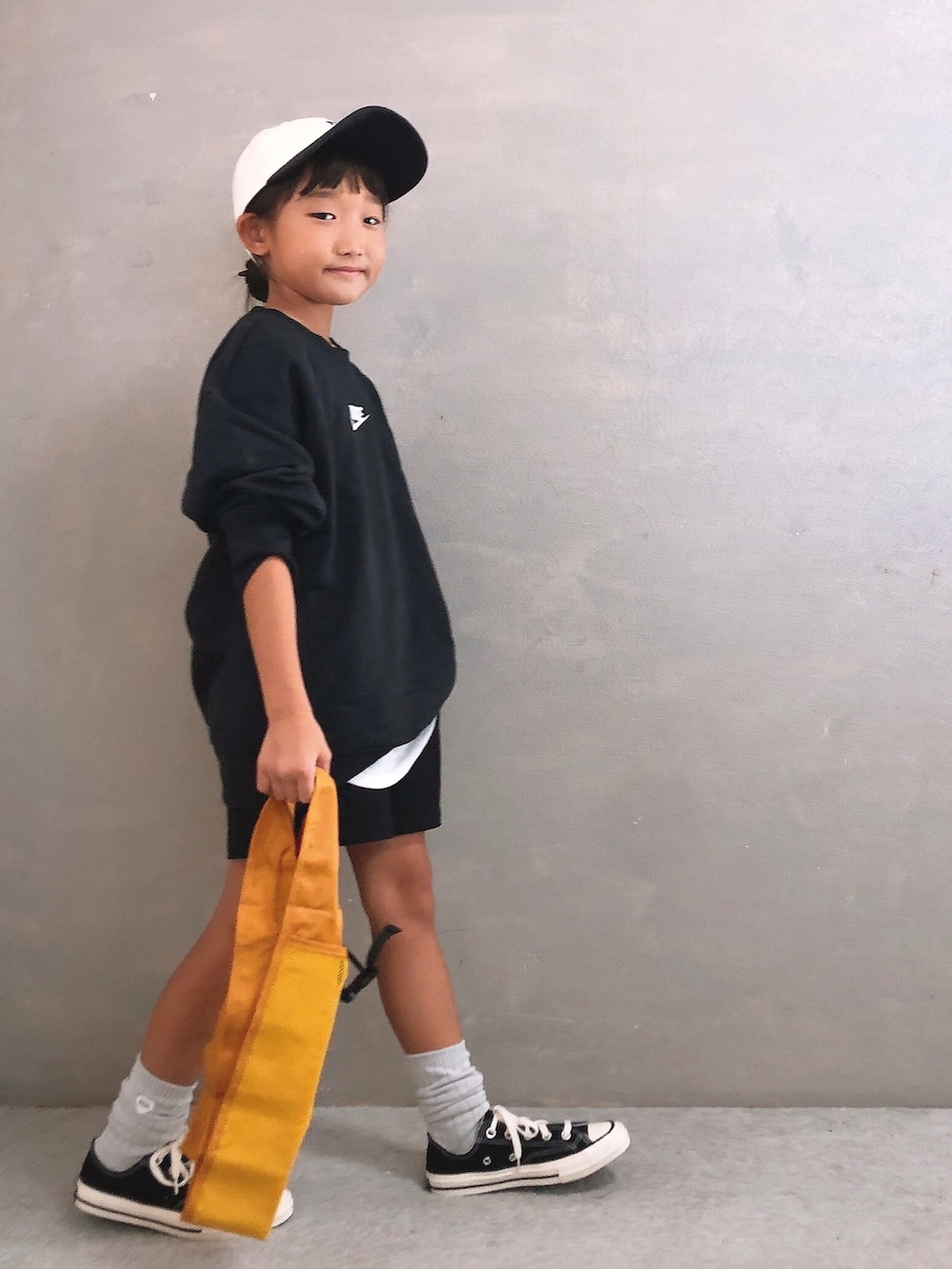 ブラック系のその他パンツ、イエロー系のエコバッグ/サブバッグ、ホワイト系のキャップを着用したキッズの秋コーディネートの2枚目の写真