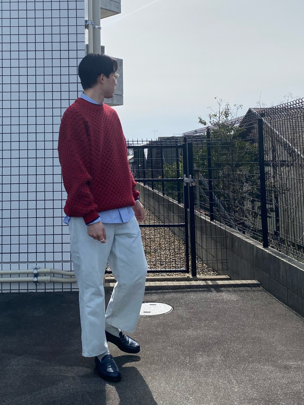 レッド系のニット/セーター、ブルー系のデニムパンツ、ブルー系のローファーを着用したメンズの春コーディネートの2枚目の写真