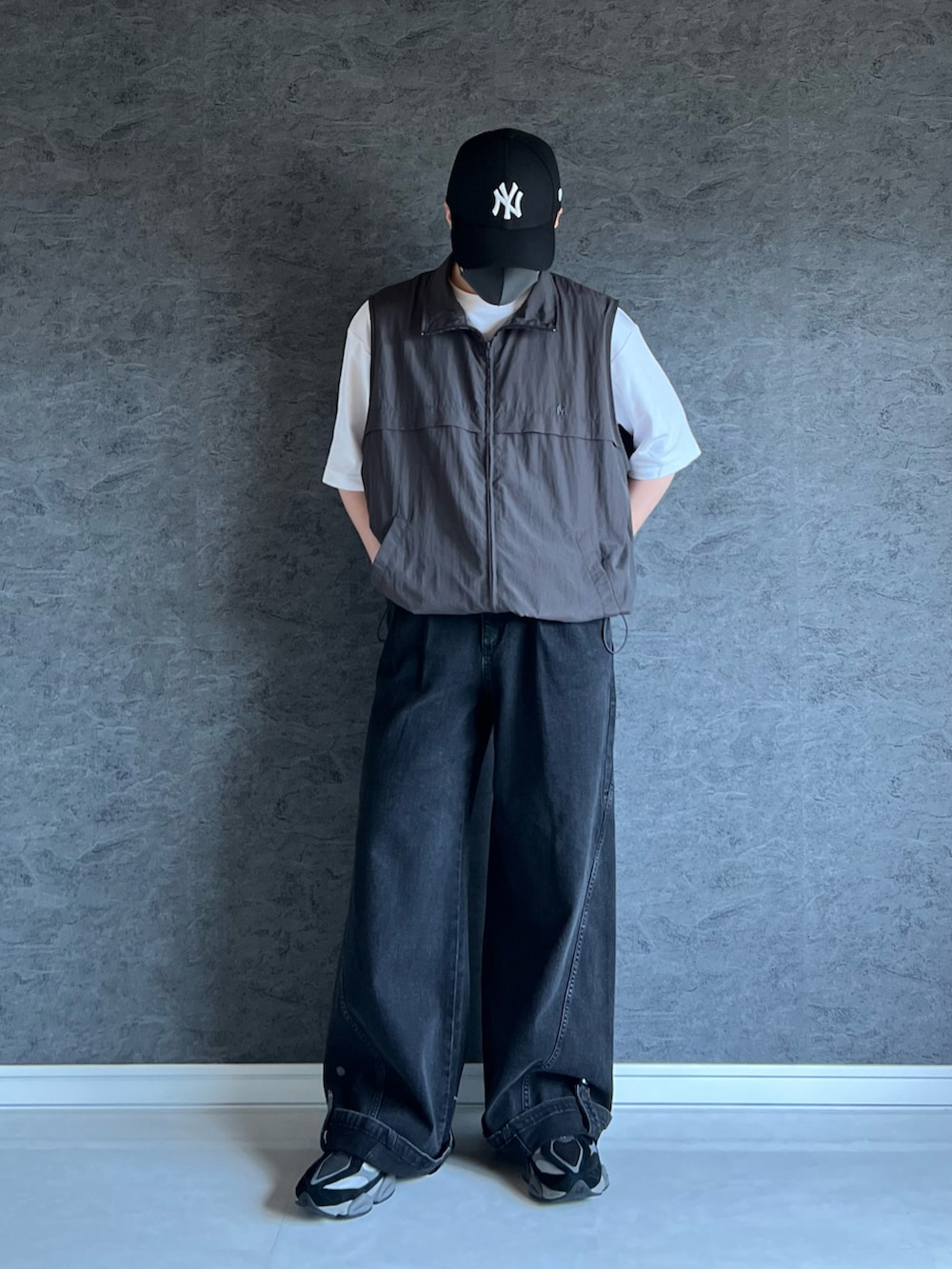 ブラック系のスニーカー、グレー系のベスト、シルバー系のブレスレットを着用したメンズの夏コーディネートの2枚目の写真