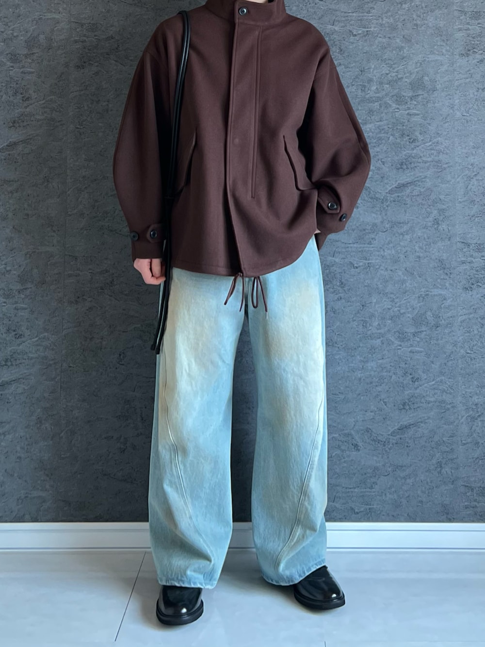 ブラウン系のモッズコート、ブラック系のショルダーバッグ、ブルー系のデニムパンツを着用したメンズの冬コーディネートの2枚目の写真