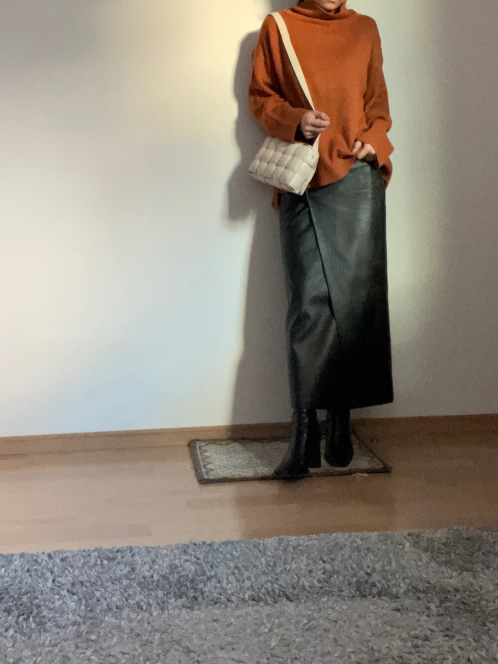 オレンジ系のニット/セーター、グレー系のチェスターコート、ブラック系のブーツを着用したレディースの秋コーディネートの2枚目の写真