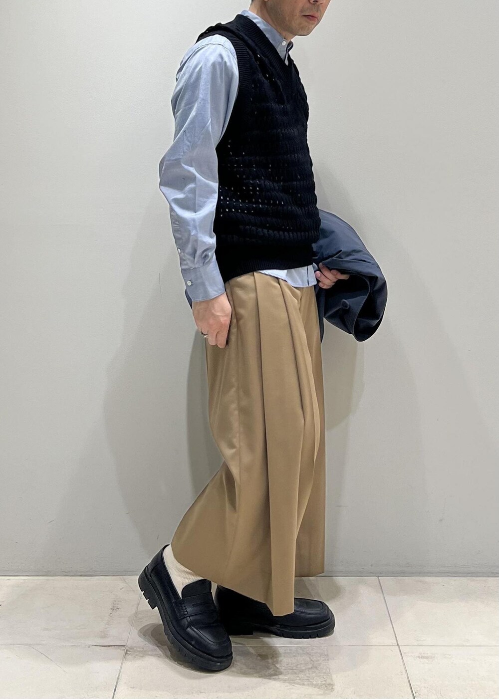 ブラック系のベスト、グレー系のステンカラーコート、イエロー系のスラックスを着用したメンズの春コーディネートの9枚目の写真