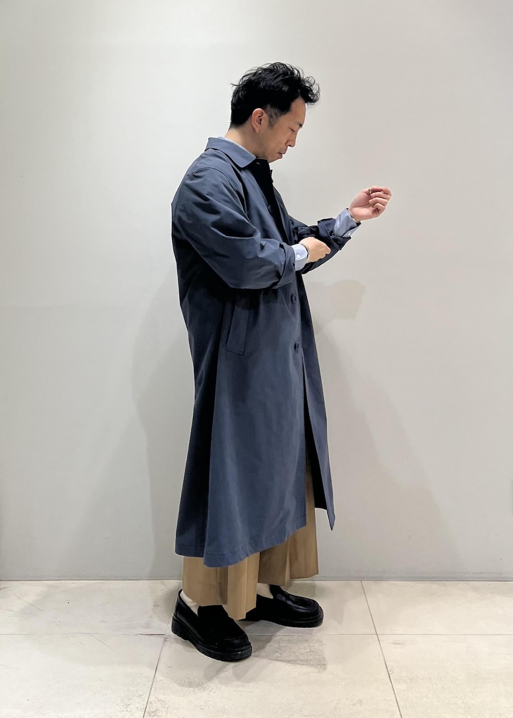 ブラック系のベスト、グレー系のステンカラーコート、イエロー系のスラックスを着用したメンズの春コーディネートの2枚目の写真