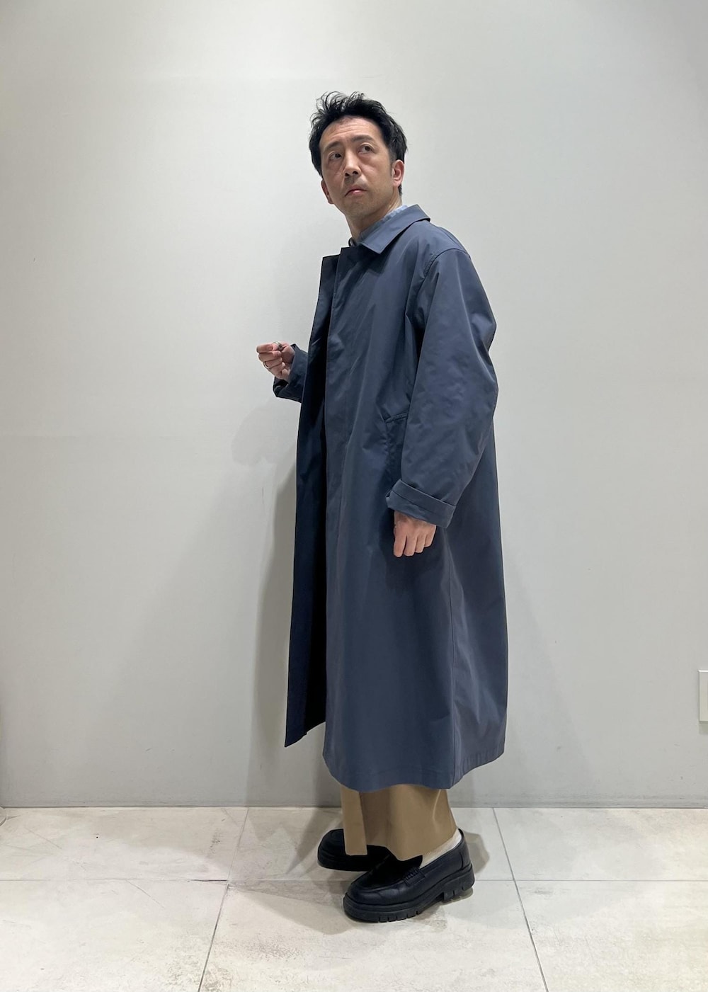 ブラック系のベスト、グレー系のステンカラーコート、イエロー系のスラックスを着用したメンズの春コーディネートの4枚目の写真