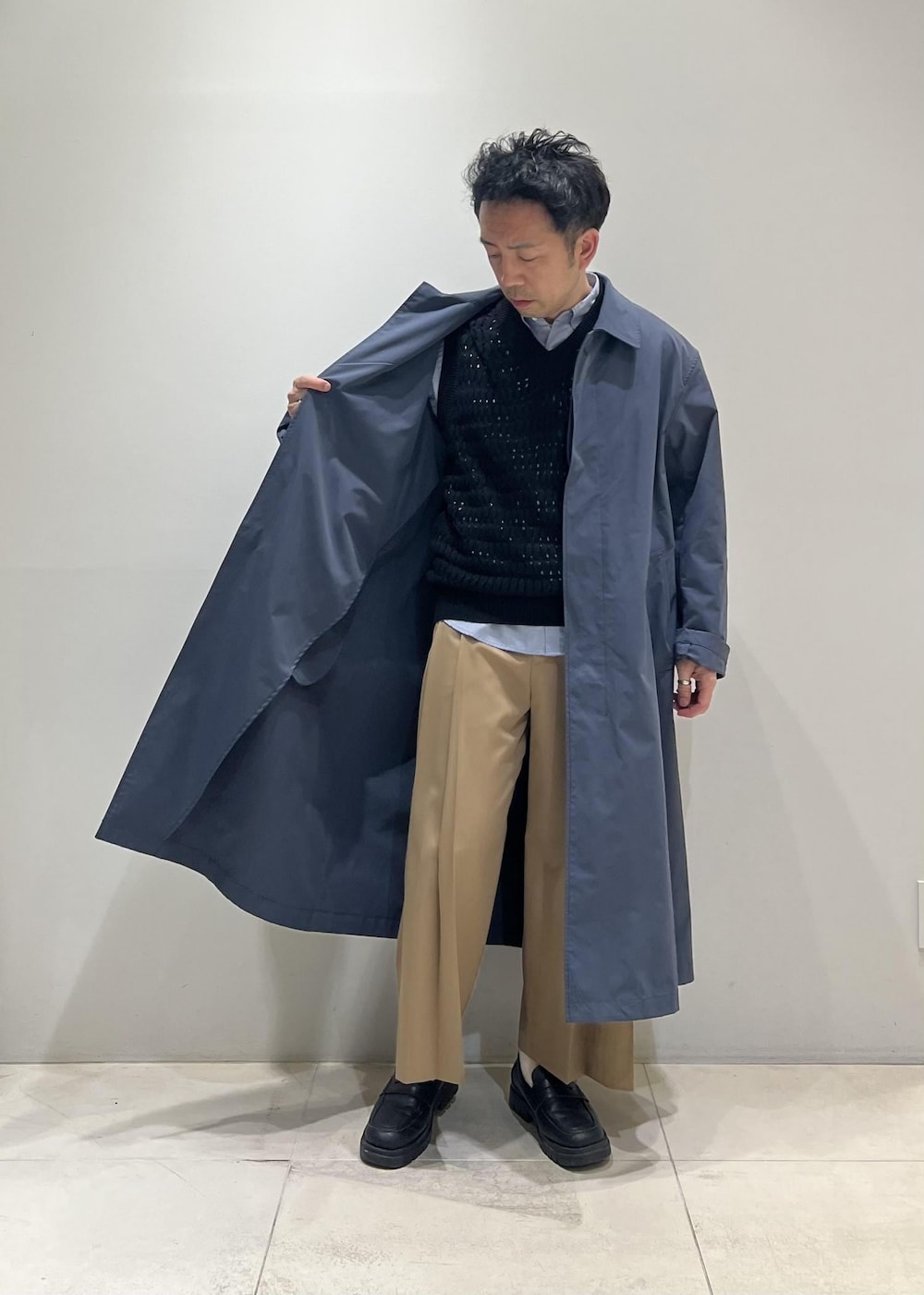 ブラック系のベスト、グレー系のステンカラーコート、イエロー系のスラックスを着用したメンズの春コーディネートの3枚目の写真