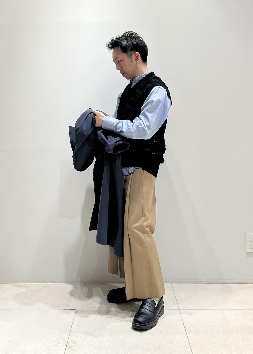 ブラック系のベスト、グレー系のステンカラーコート、イエロー系のスラックスを着用したメンズの春コーディネートの6枚目の写真