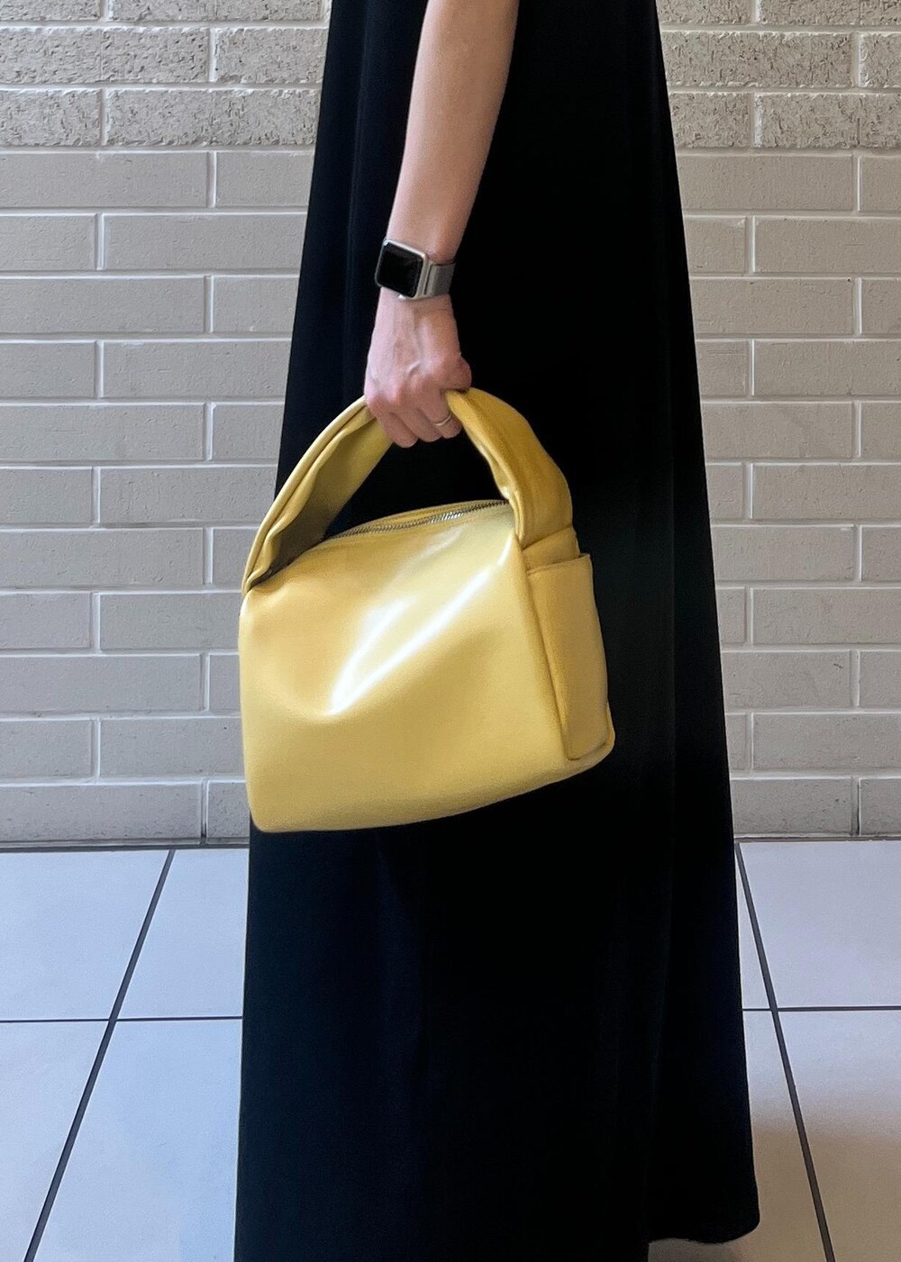 イエロー系のハンドバッグ、ブラック系のワンピースを着用したレディースの夏コーディネートの5枚目の写真