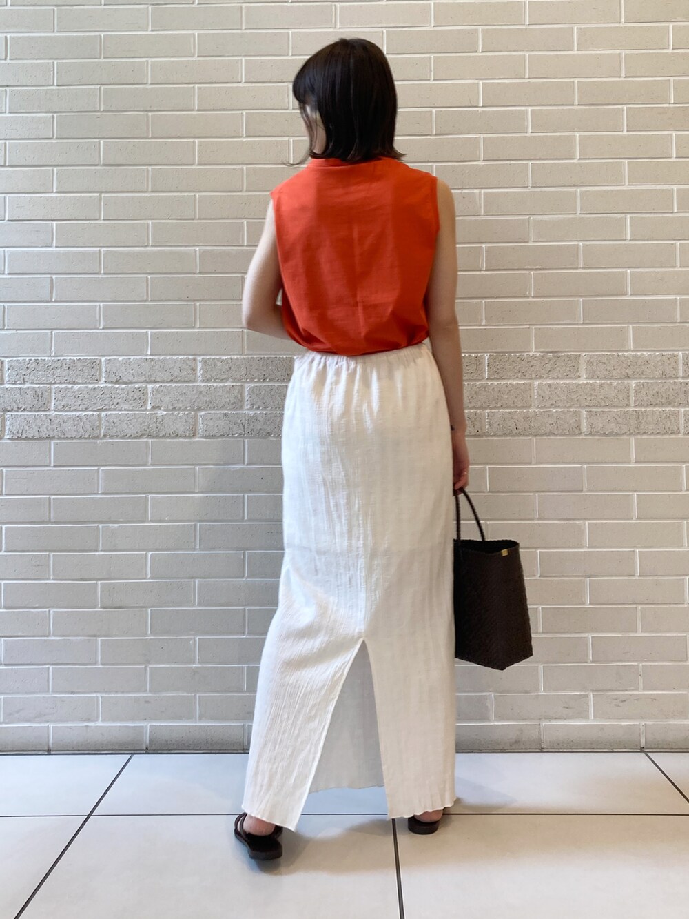 オレンジ系のTシャツ/カットソー、ブラウン系のサンダル、ホワイト系のスカートを着用したレディースの春コーディネートの3枚目の写真