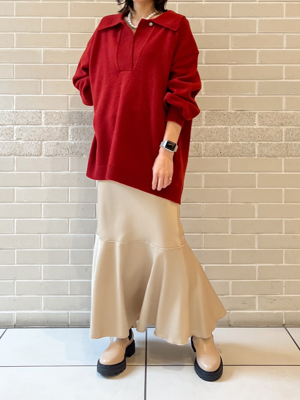 レッド系のニット/セーター、ベージュ系のスカート、ベージュ系のブーツを着用したレディースの秋コーディネートの2枚目の写真