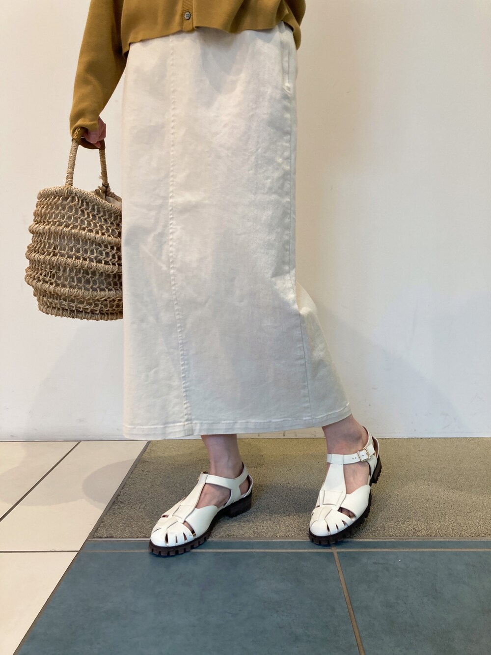 イエロー系のカーディガン/ボレロ、ベージュ系のかごバッグ、ホワイト系のスカートを着用したレディースの春コーディネートの4枚目の写真