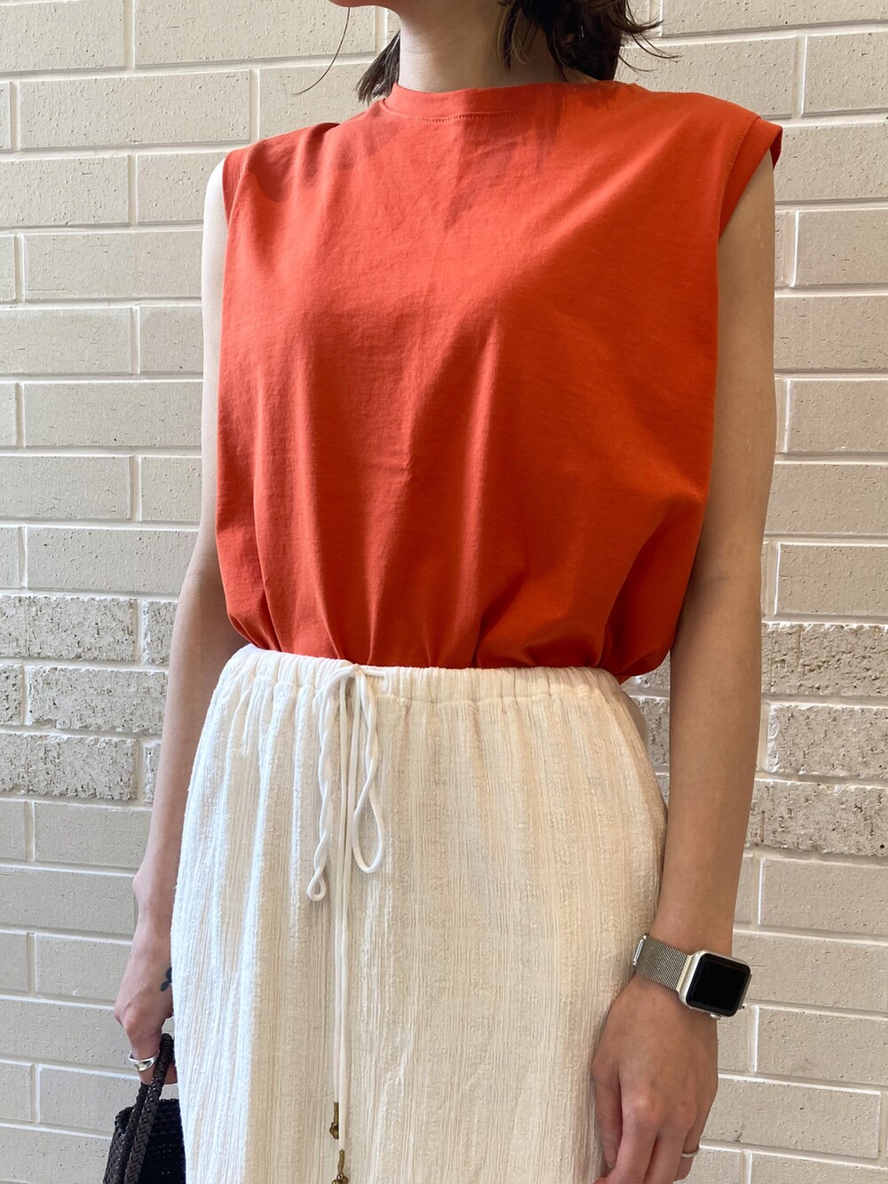 オレンジ系のTシャツ/カットソー、ブラウン系のサンダル、ホワイト系のスカートを着用したレディースの春コーディネートの4枚目の写真