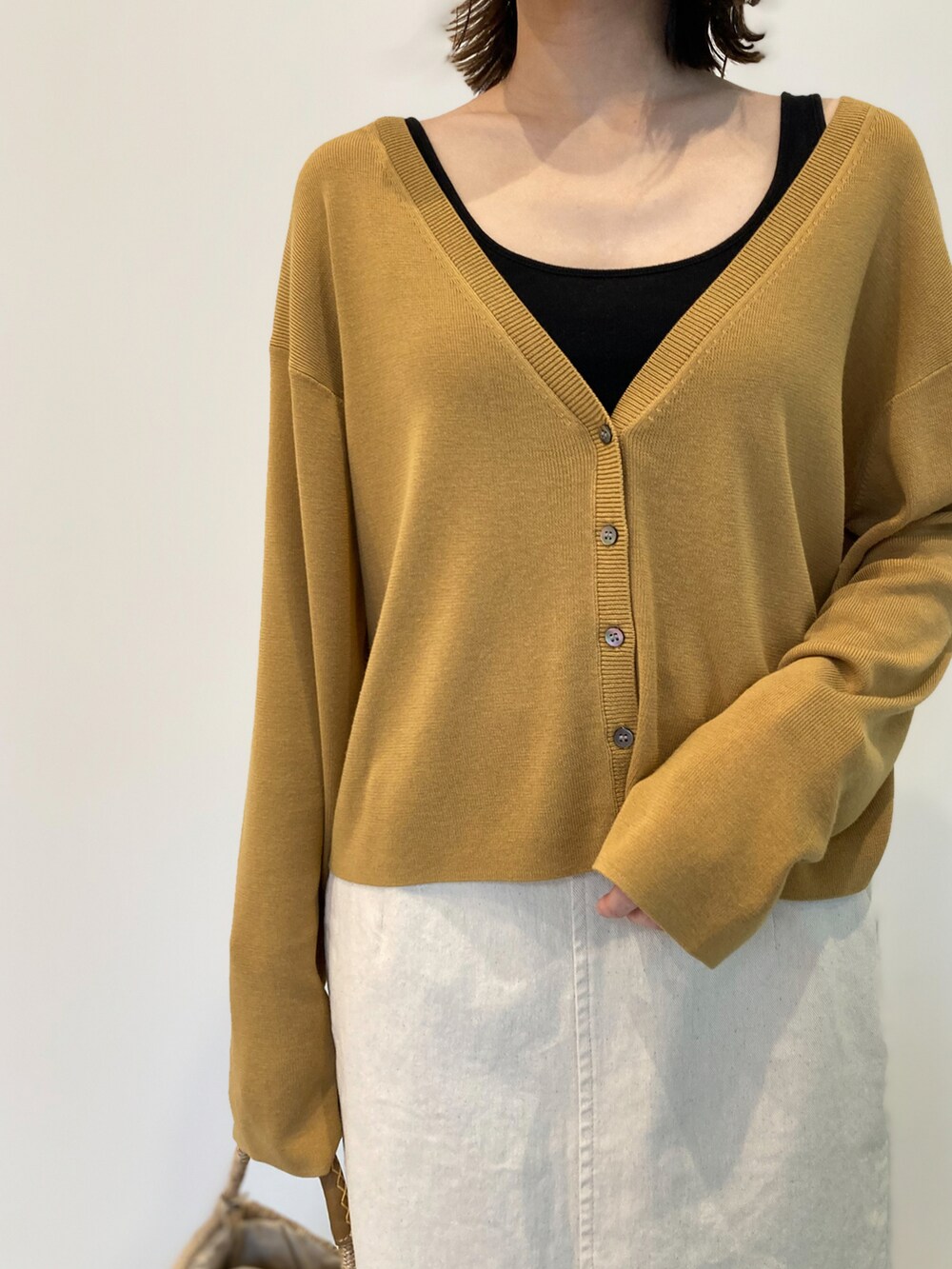 イエロー系のカーディガン/ボレロ、ベージュ系のかごバッグ、ホワイト系のスカートを着用したレディースの春コーディネートの2枚目の写真