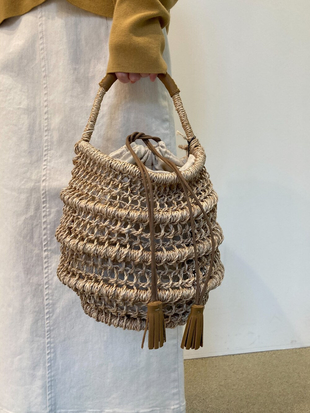 イエロー系のカーディガン/ボレロ、ベージュ系のかごバッグ、ホワイト系のスカートを着用したレディースの春コーディネートの5枚目の写真