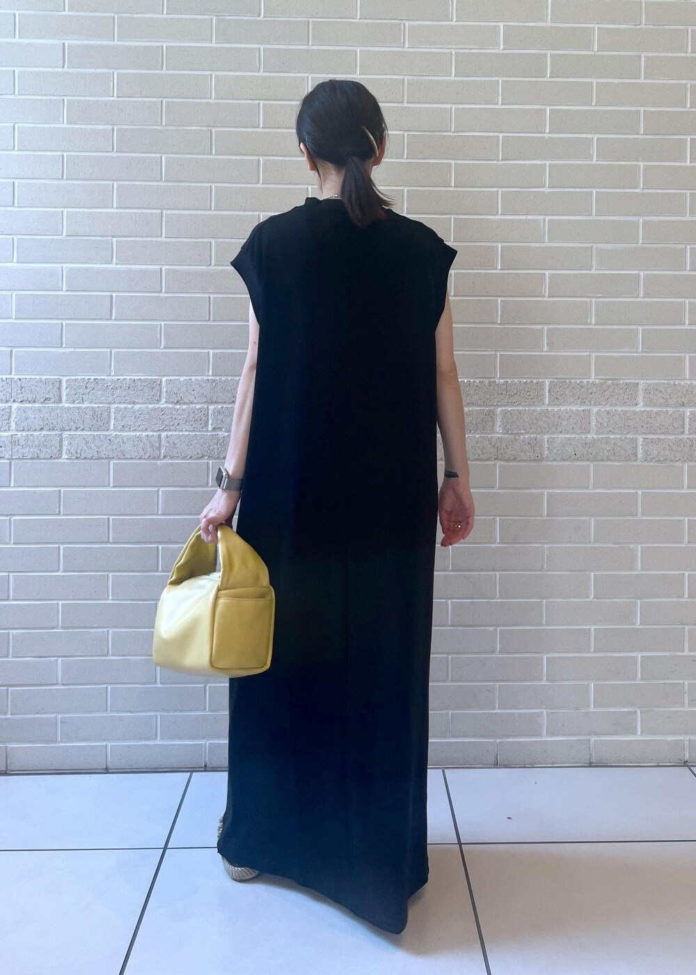 イエロー系のハンドバッグ、ブラック系のワンピースを着用したレディースの夏コーディネートの3枚目の写真