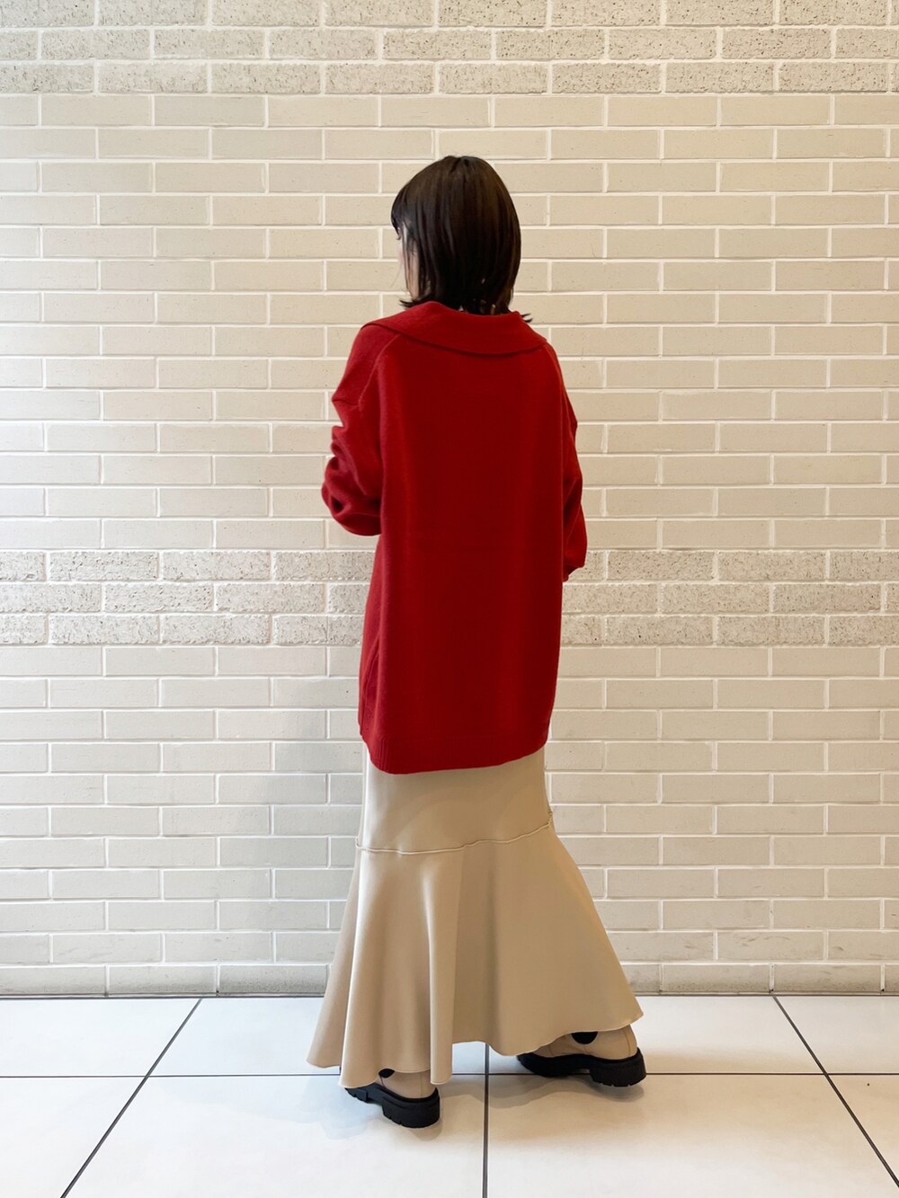 レッド系のニット/セーター、ベージュ系のスカート、ベージュ系のブーツを着用したレディースの秋コーディネートの4枚目の写真