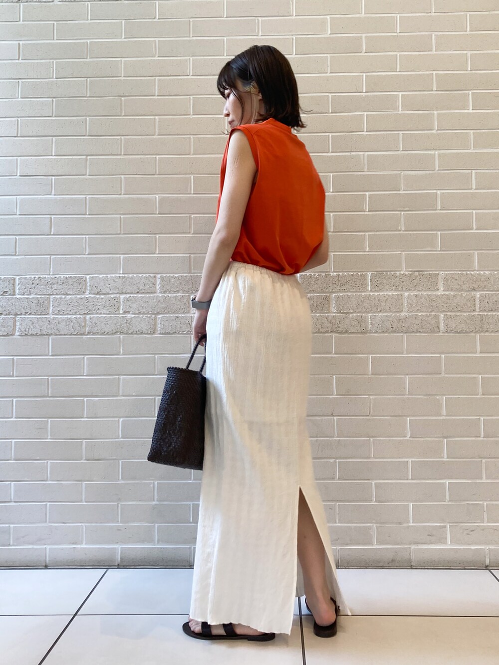 オレンジ系のTシャツ/カットソー、ブラウン系のサンダル、ホワイト系のスカートを着用したレディースの春コーディネートの2枚目の写真