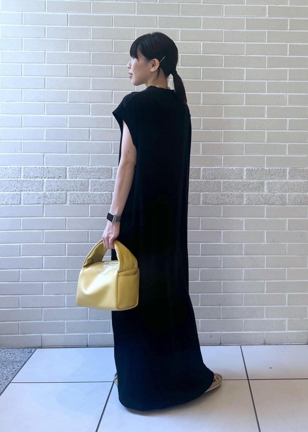 イエロー系のハンドバッグ、ブラック系のワンピースを着用したレディースの夏コーディネートの2枚目の写真