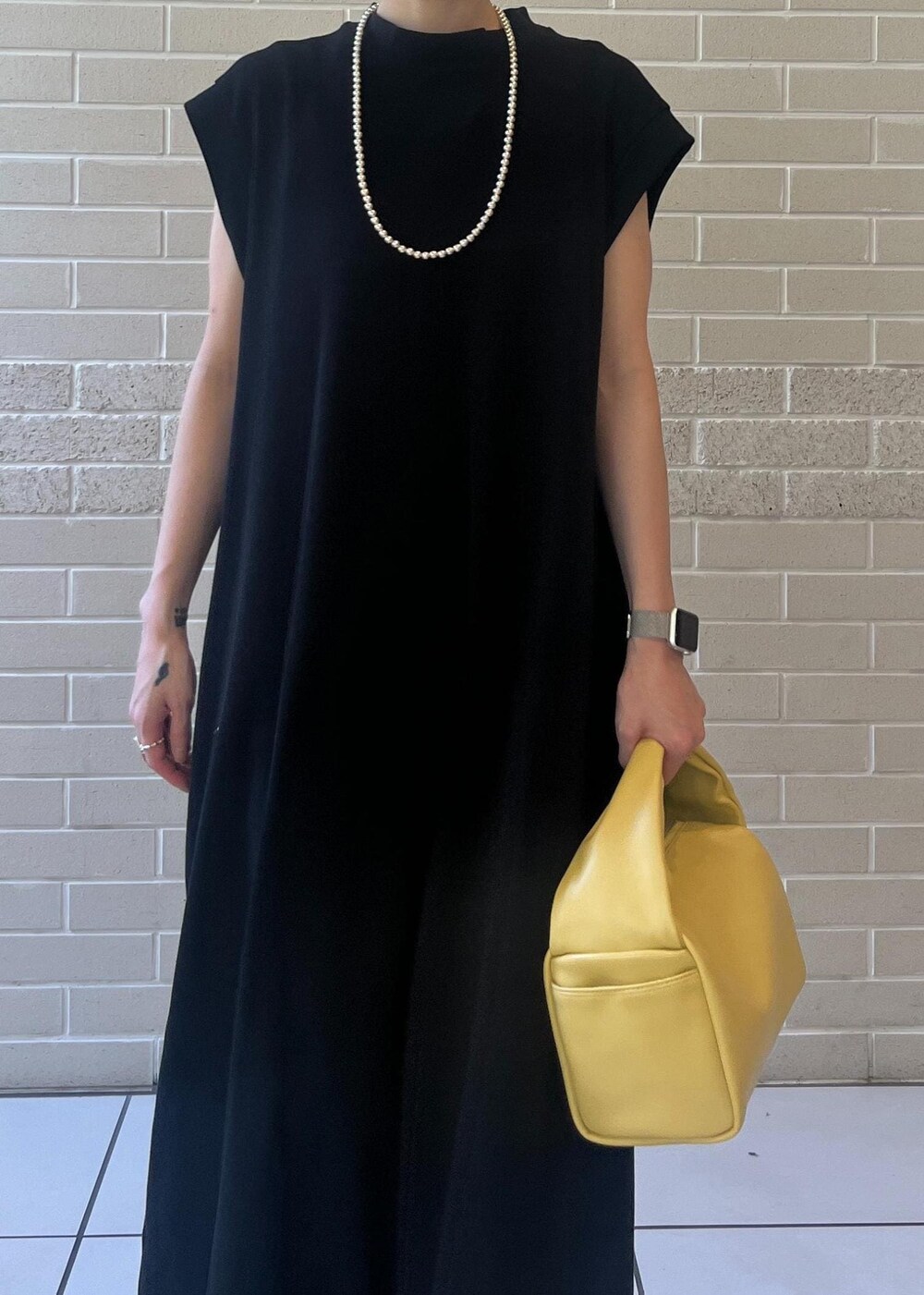 イエロー系のハンドバッグ、ブラック系のワンピースを着用したレディースの夏コーディネートの4枚目の写真