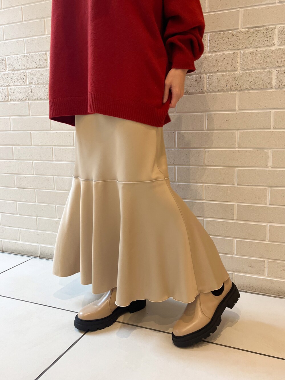レッド系のニット/セーター、ベージュ系のスカート、ベージュ系のブーツを着用したレディースの秋コーディネートの3枚目の写真