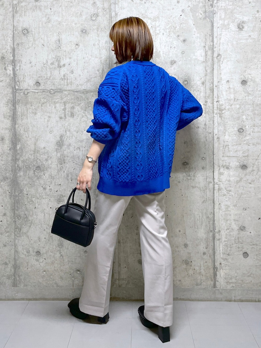 ブルー系のニット/セーター、ブラック系のボストンバッグ、ベージュ系のスラックスを着用したレディースの冬コーディネートの3枚目の写真