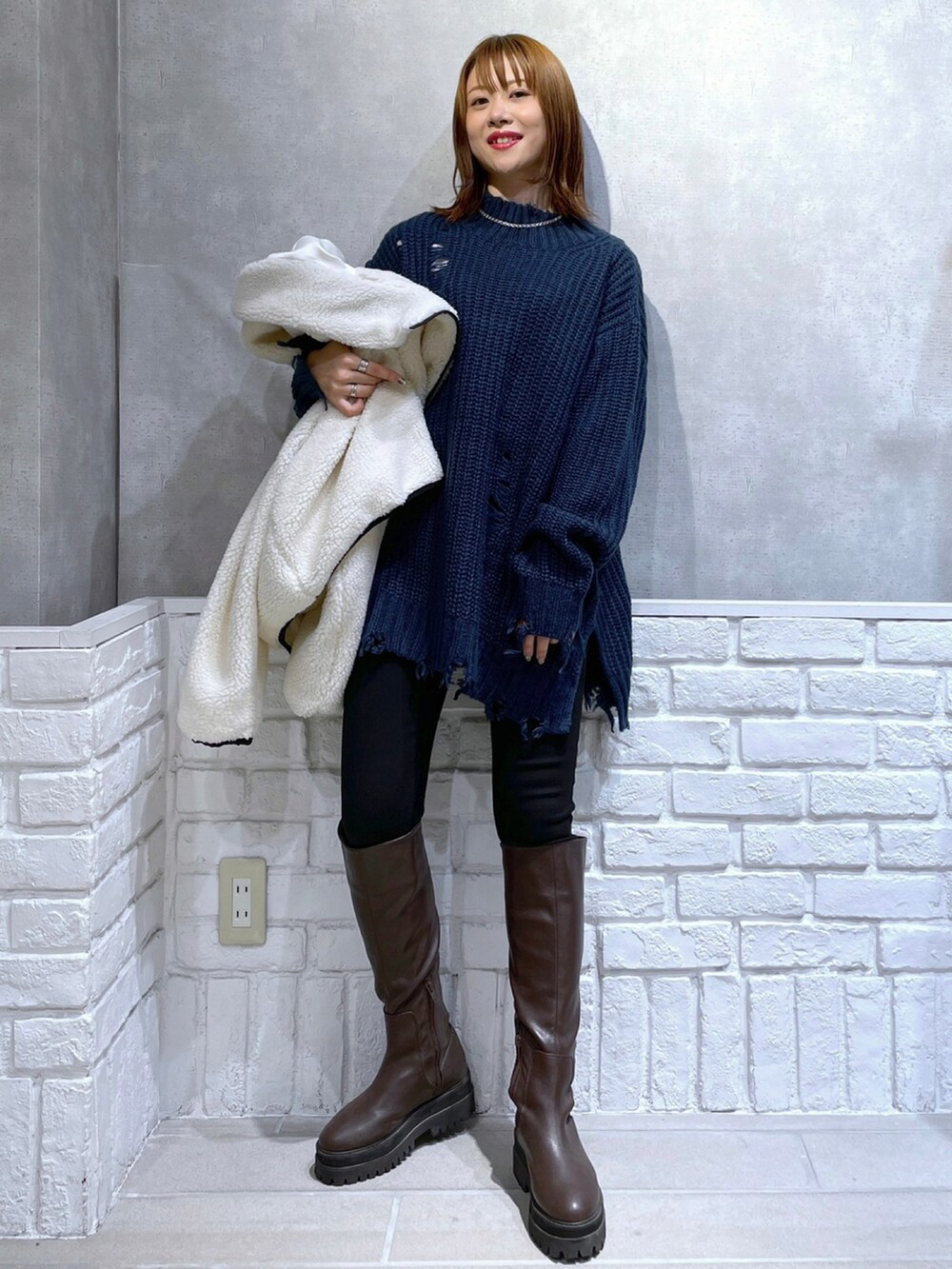 ブラック系のデニムパンツ、ブラウン系のブーツ、ホワイト系のブルゾンを着用したレディースの秋コーディネートの2枚目の写真