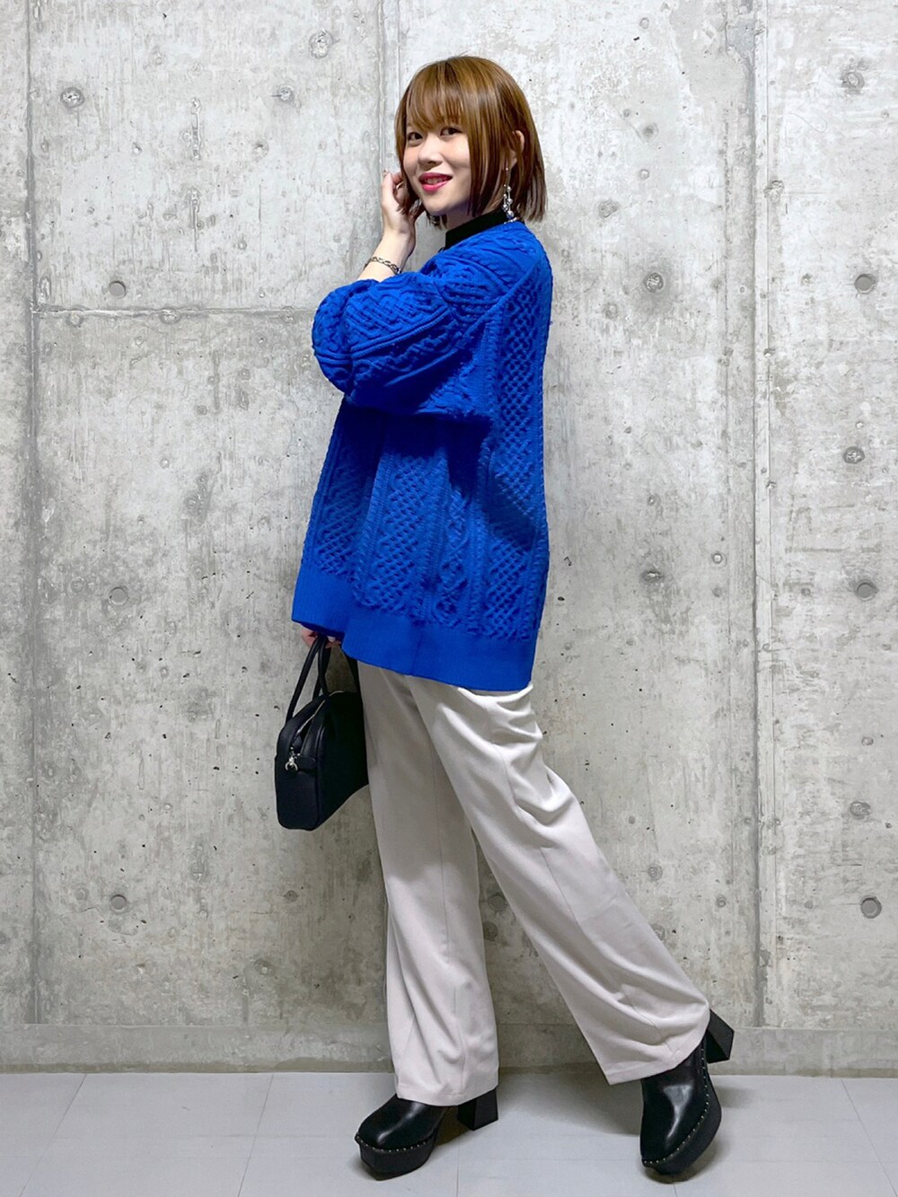 ブルー系のニット/セーター、ブラック系のボストンバッグ、ベージュ系のスラックスを着用したレディースの冬コーディネートの2枚目の写真