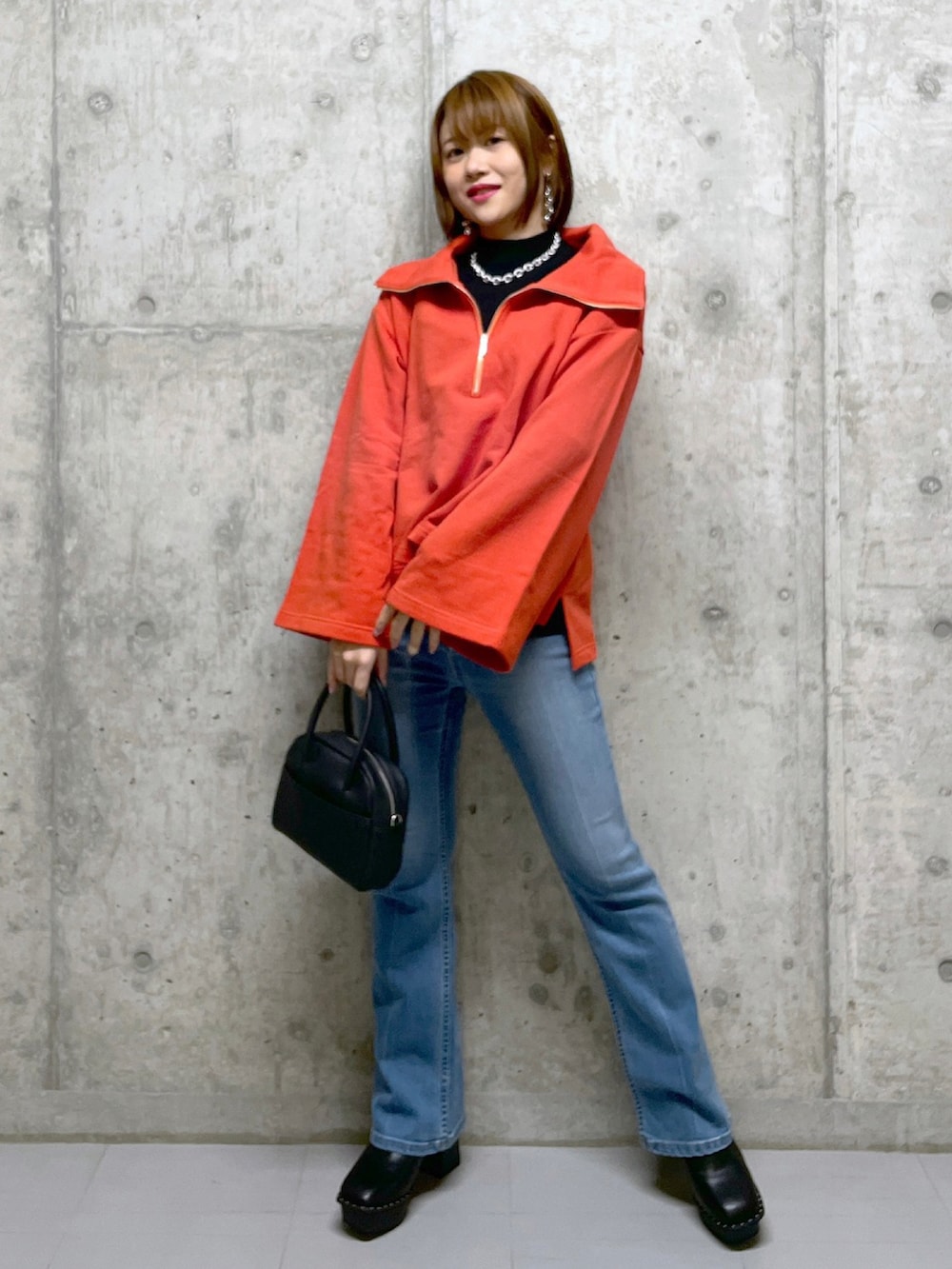 オレンジ系のスウェット、ブラック系のボストンバッグ、ホワイト系のその他パンツを着用したレディースの冬コーディネートの2枚目の写真