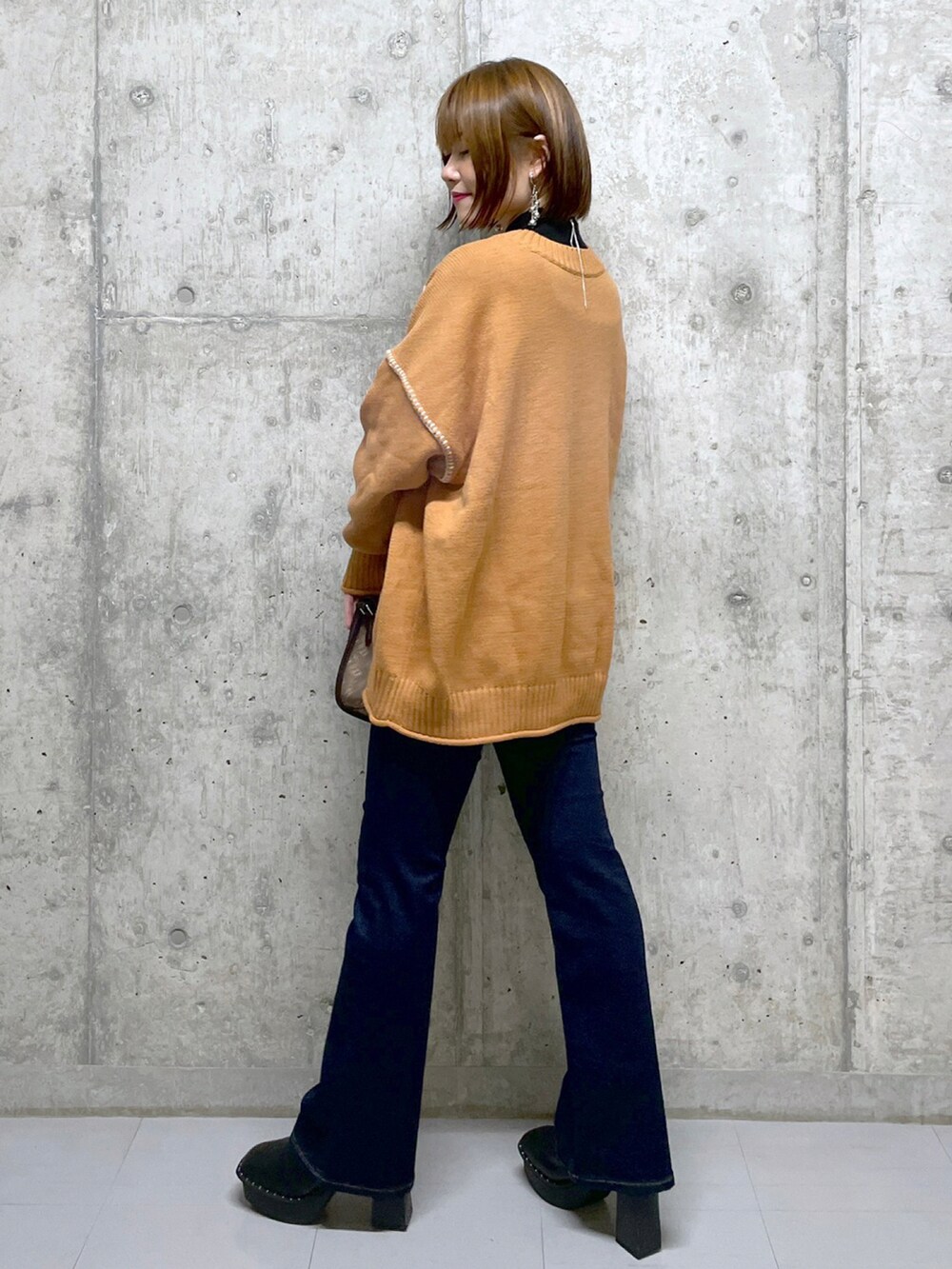 オレンジ系のニット/セーター、ブラック系のニット/セーター、ブラウン系のショルダーバッグを着用したレディースの冬コーディネートの2枚目の写真