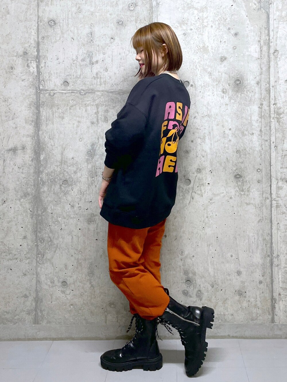 オレンジ系のスラックス、ブラック系のブーツ、ブラック系のスウェットを着用したレディースの冬コーディネートの2枚目の写真