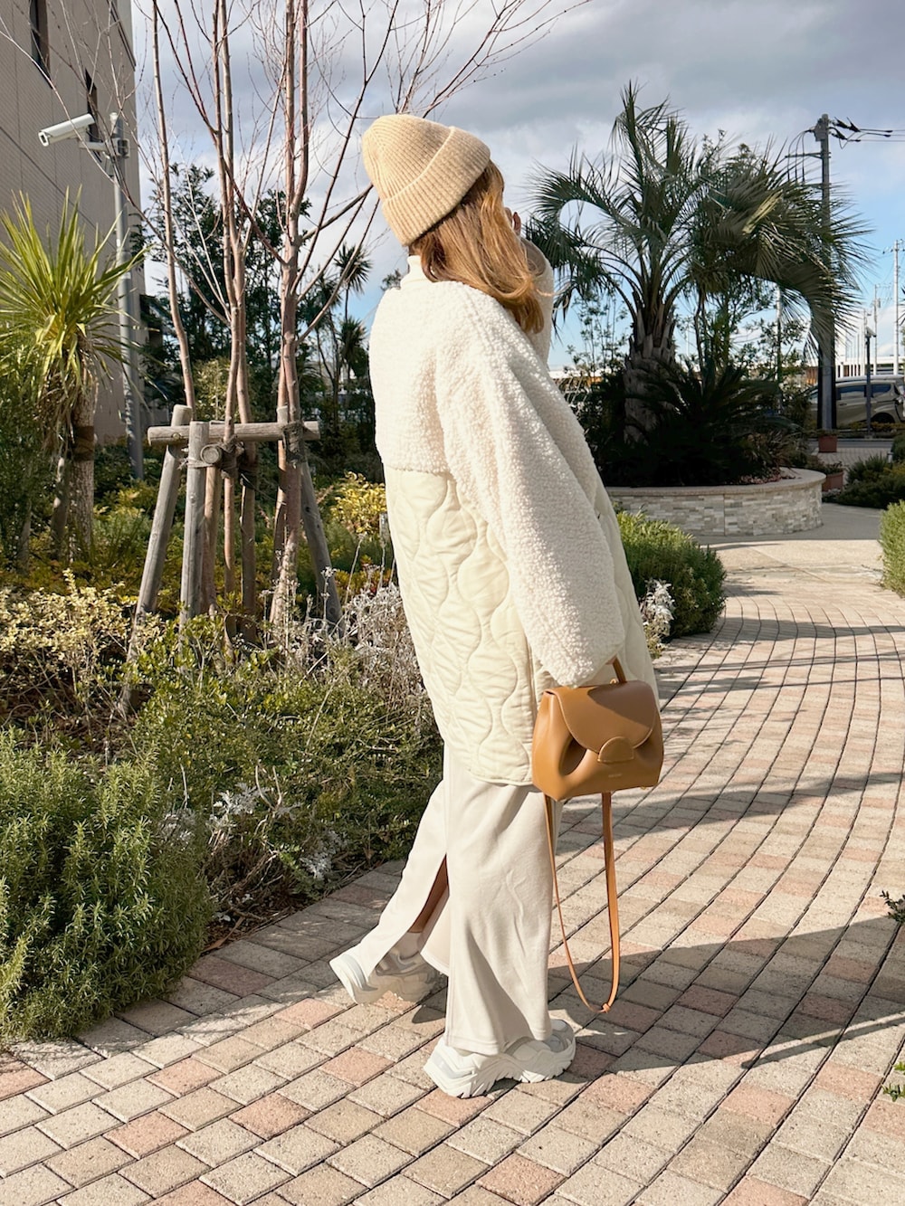 ベージュ系のワンピース、ベージュ系のバッグ、ホワイト系のスニーカーを着用したレディースの冬コーディネートの2枚目の写真