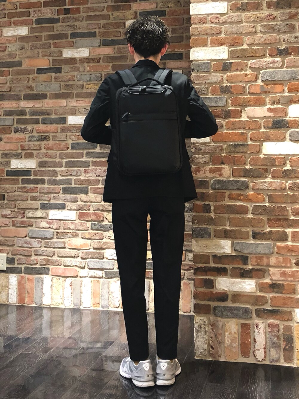 ブラック系のスーツセット、ブラック系のバックパック/リュック、ベージュ系のTシャツ/カットソーを着用したメンズの春コーディネートの2枚目の写真