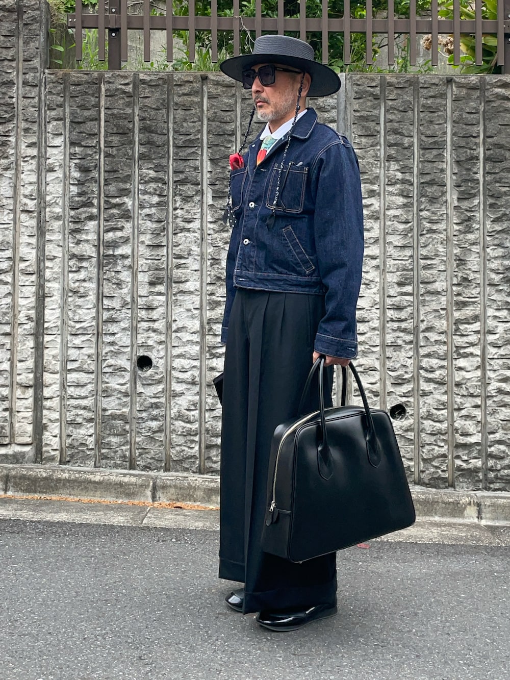 ブラック系のバッグ、ブルー系のデニムジャケット、レッド系のポケットチーフを着用したメンズの春コーディネートの2枚目の写真
