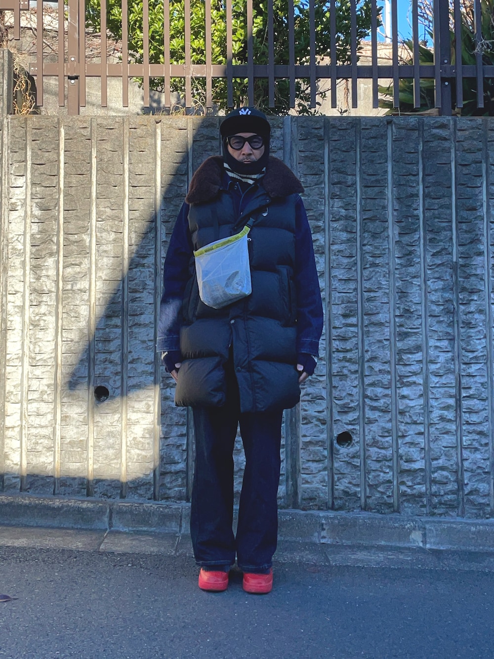 ブラック系のダウンベスト、ブルー系のデニムパンツ、レッド系のスニーカーを着用したメンズの冬コーディネートの2枚目の写真