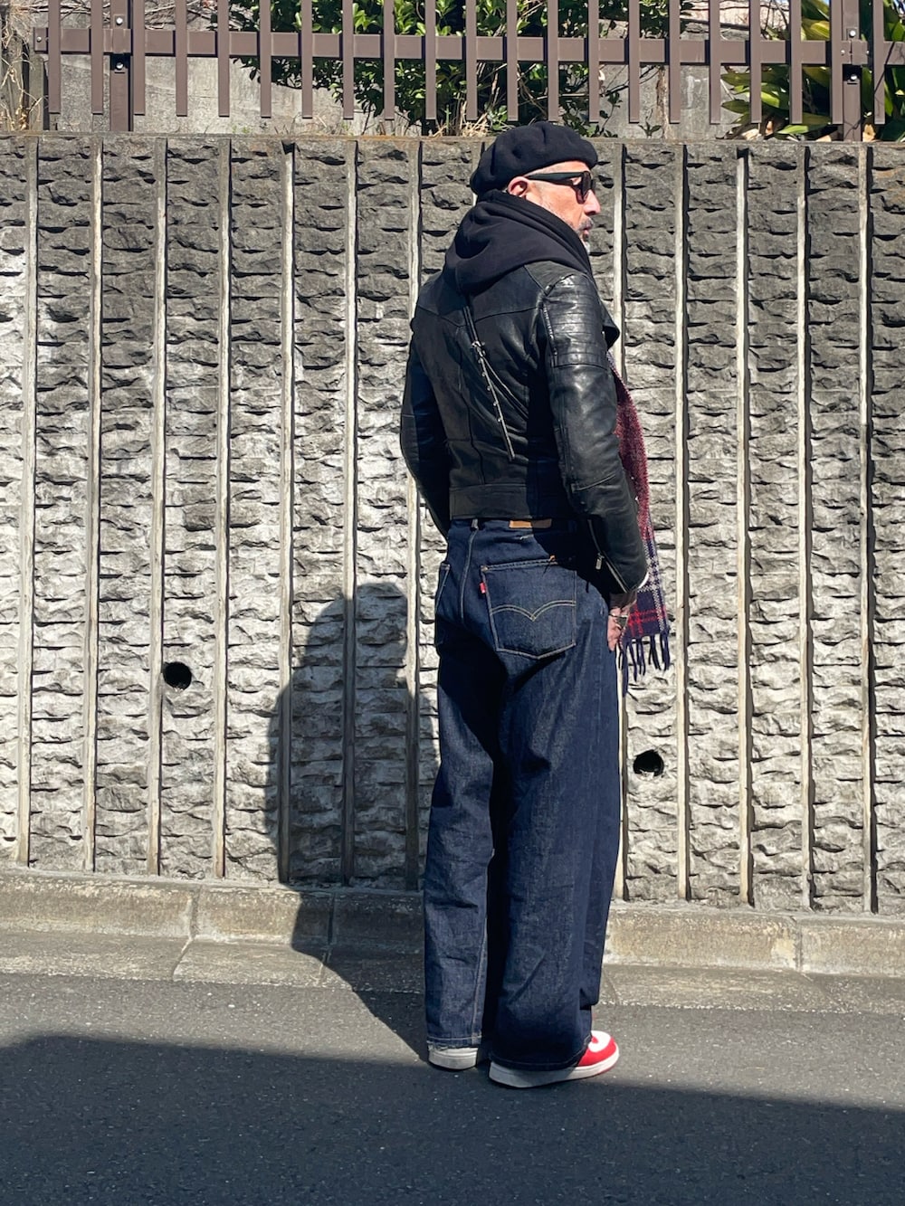 ブルー系のデニムパンツ、ホワイト系のスニーカー、ブラック系のライダースジャケットを着用したメンズの春コーディネートの2枚目の写真