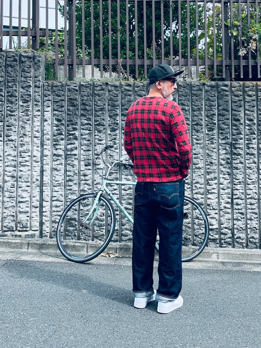 レッド系のTシャツ/カットソー、ブルー系のデニムパンツ、ホワイト系のスニーカーを着用したメンズの秋コーディネートの2枚目の写真