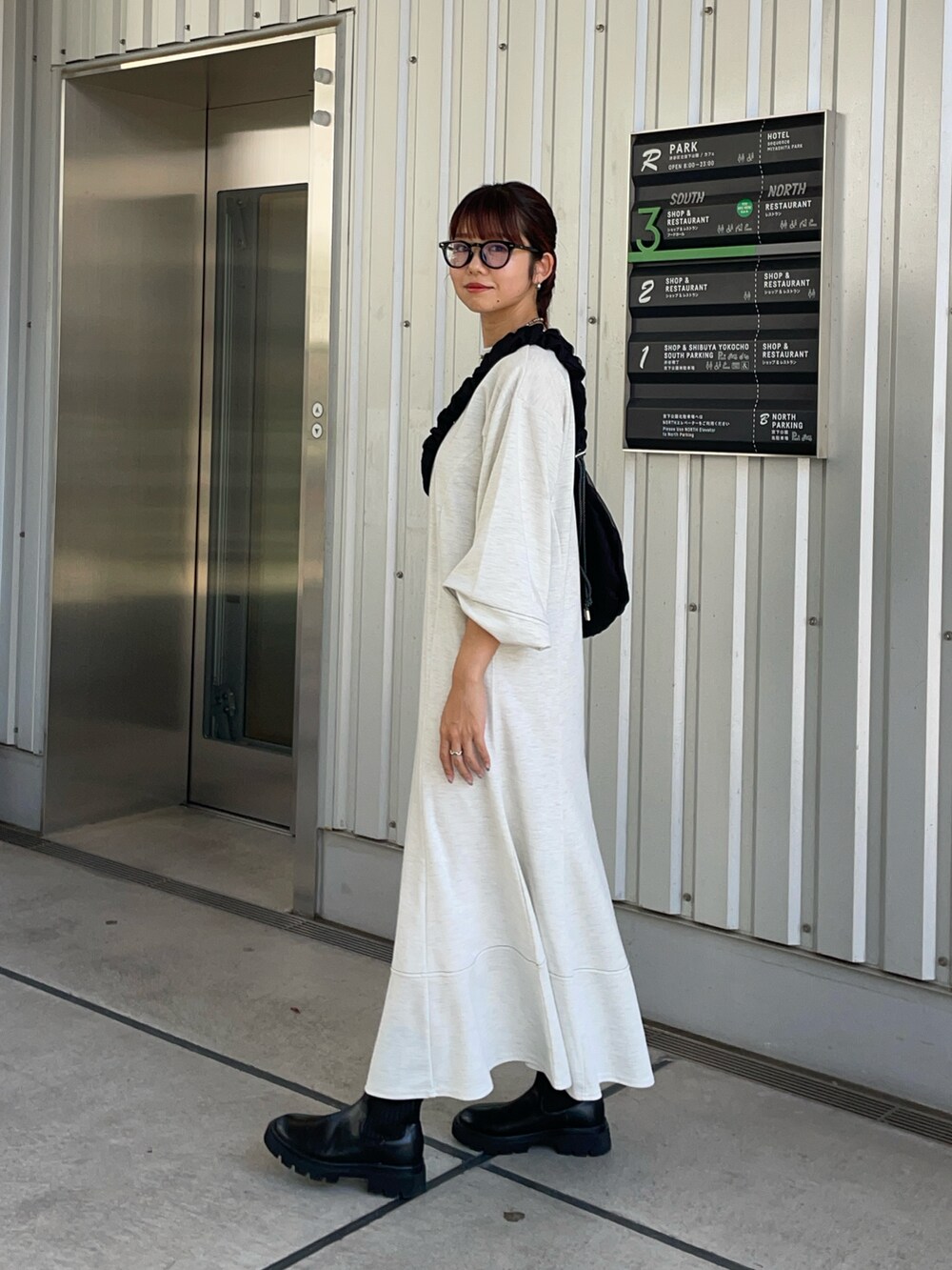 グレー系のワンピース、ブラック系のブーツ、ブラック系のショルダーバッグを着用したレディースの秋コーディネートの2枚目の写真