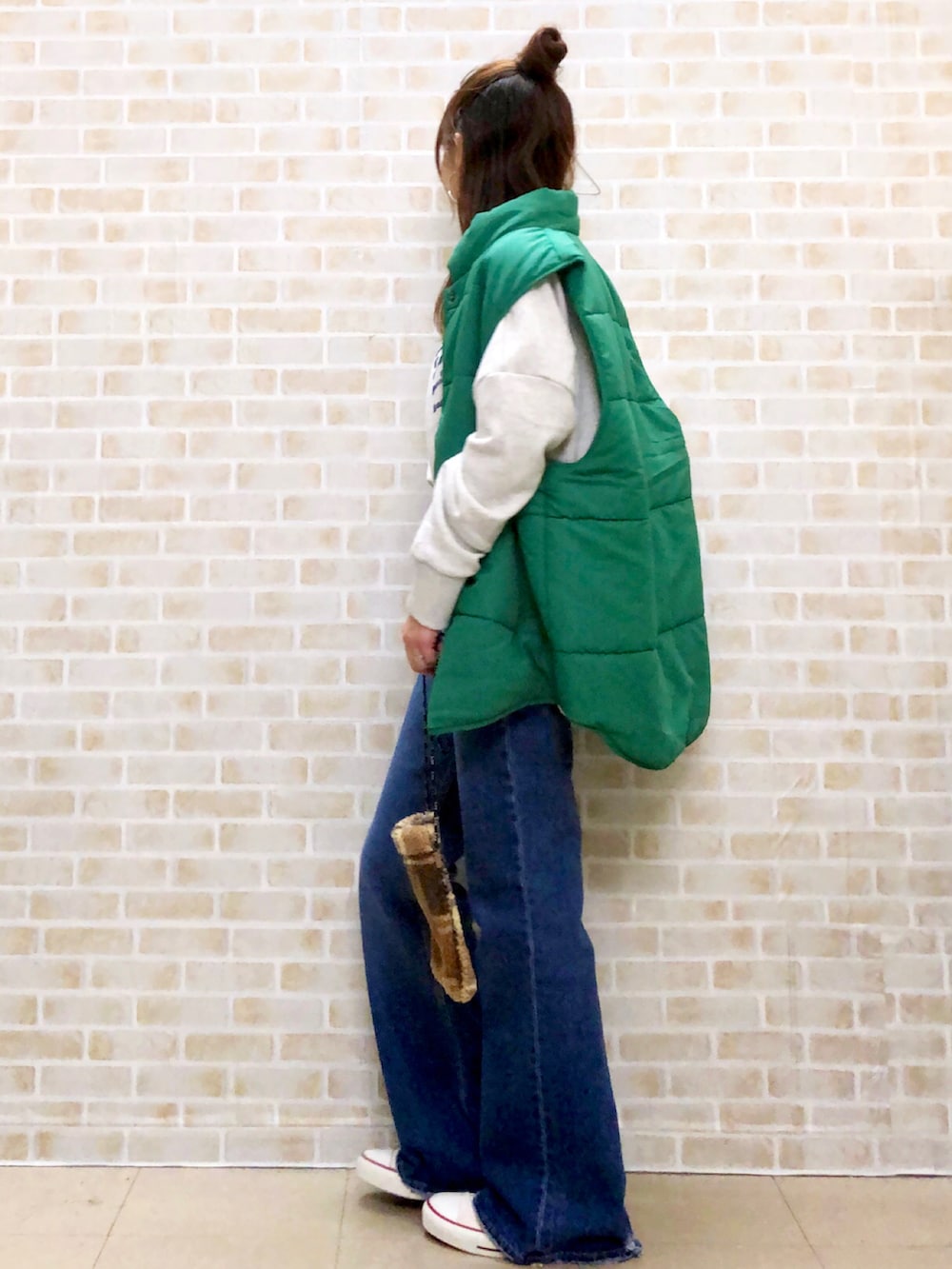グリーン系のベスト、ブルー系のデニムパンツ、ベージュ系のショルダーバッグを着用したレディースの秋コーディネートの3枚目の写真