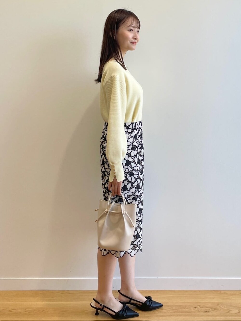 イエロー系のニット/セーター、グレー系のスカート、ホワイト系のショルダーバッグを着用したレディースの春コーディネートの2枚目の写真