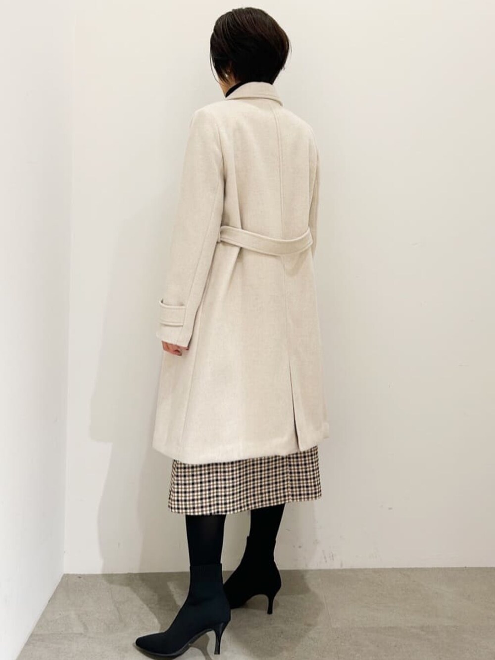 ベージュ系のチェスターコート、ブラック系のニット/セーター、ベージュ系のワンピースを着用したレディースの秋コーディネートの2枚目の写真