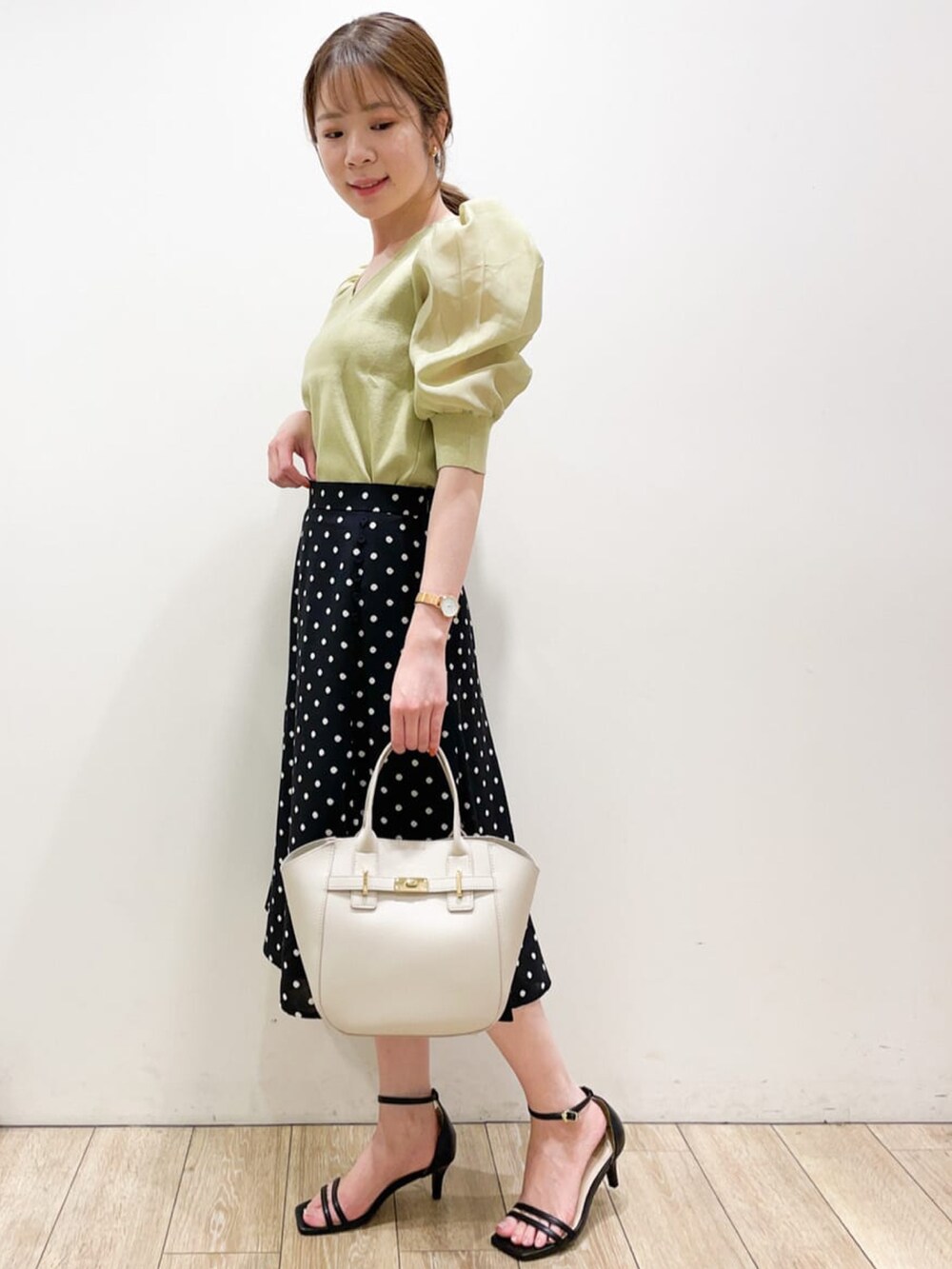 イエロー系のニット/セーター、ブラック系のスカート、ベージュ系のトートバッグを着用したレディースの夏コーディネートの2枚目の写真