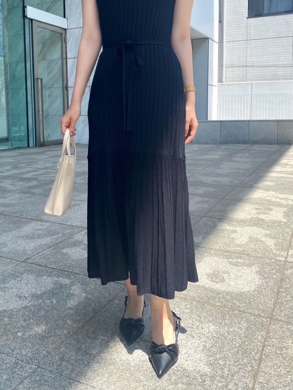 ブラック系のワンピース、ブラック系のパンプス、ゴールド系のピアス（両耳用）を着用したレディースの春コーディネートの6枚目の写真