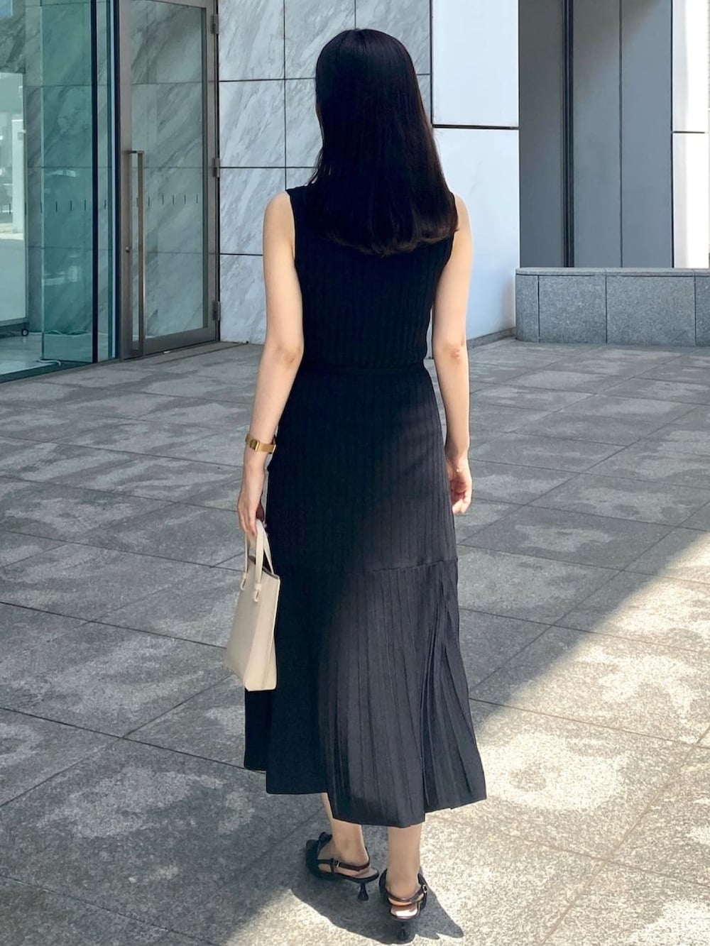 ブラック系のワンピース、ブラック系のパンプス、ゴールド系のピアス（両耳用）を着用したレディースの春コーディネートの3枚目の写真