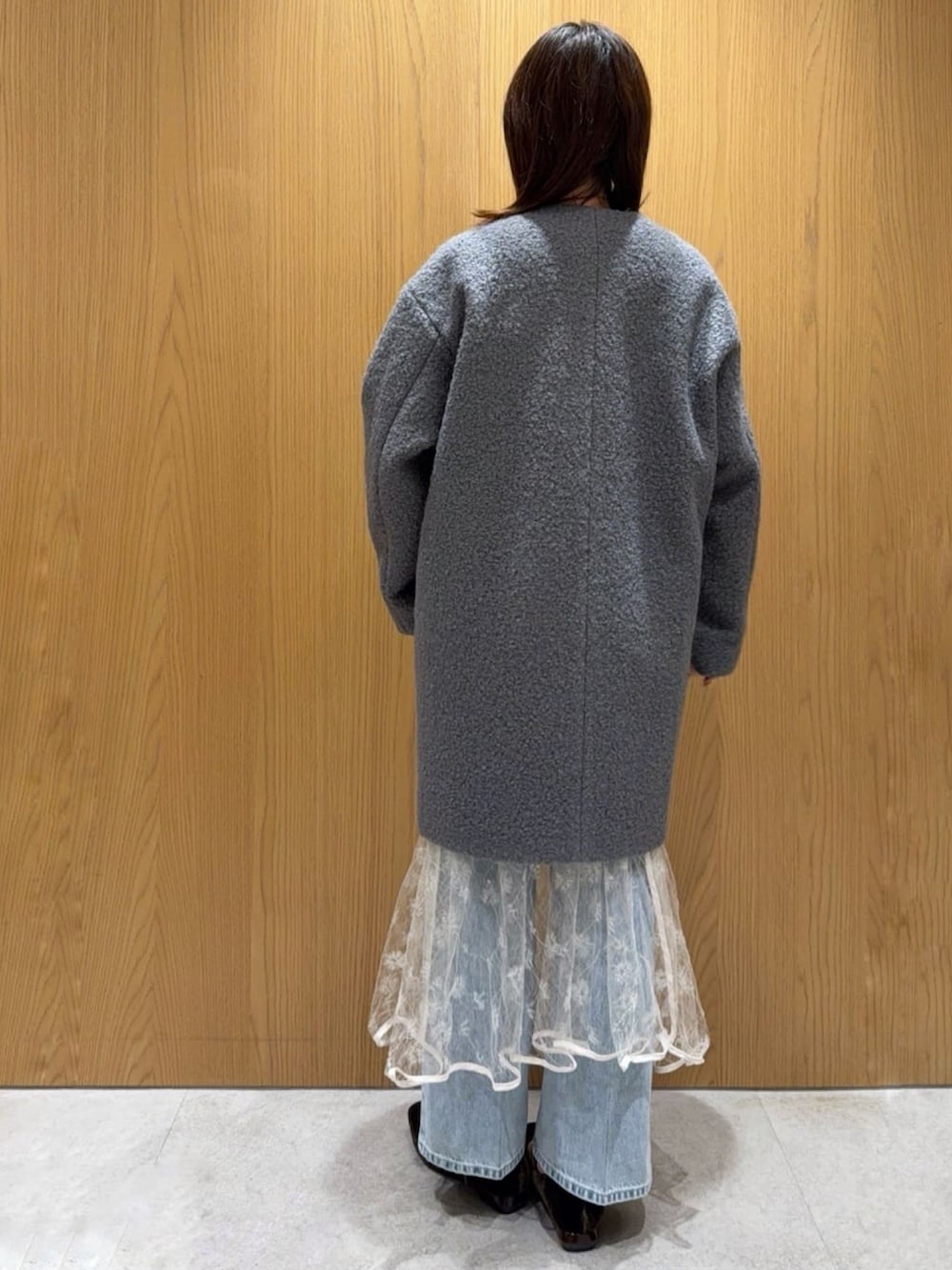 グレー系のノーカラーコート、ホワイト系のカーディガン/ボレロ、ホワイト系のスカートを着用したレディースの秋コーディネートの3枚目の写真