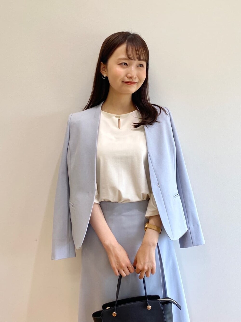 ブルー系のノーカラージャケット、ブルー系のスカート、ブラック系のハンドバッグを着用したレディースの春コーディネートの4枚目の写真