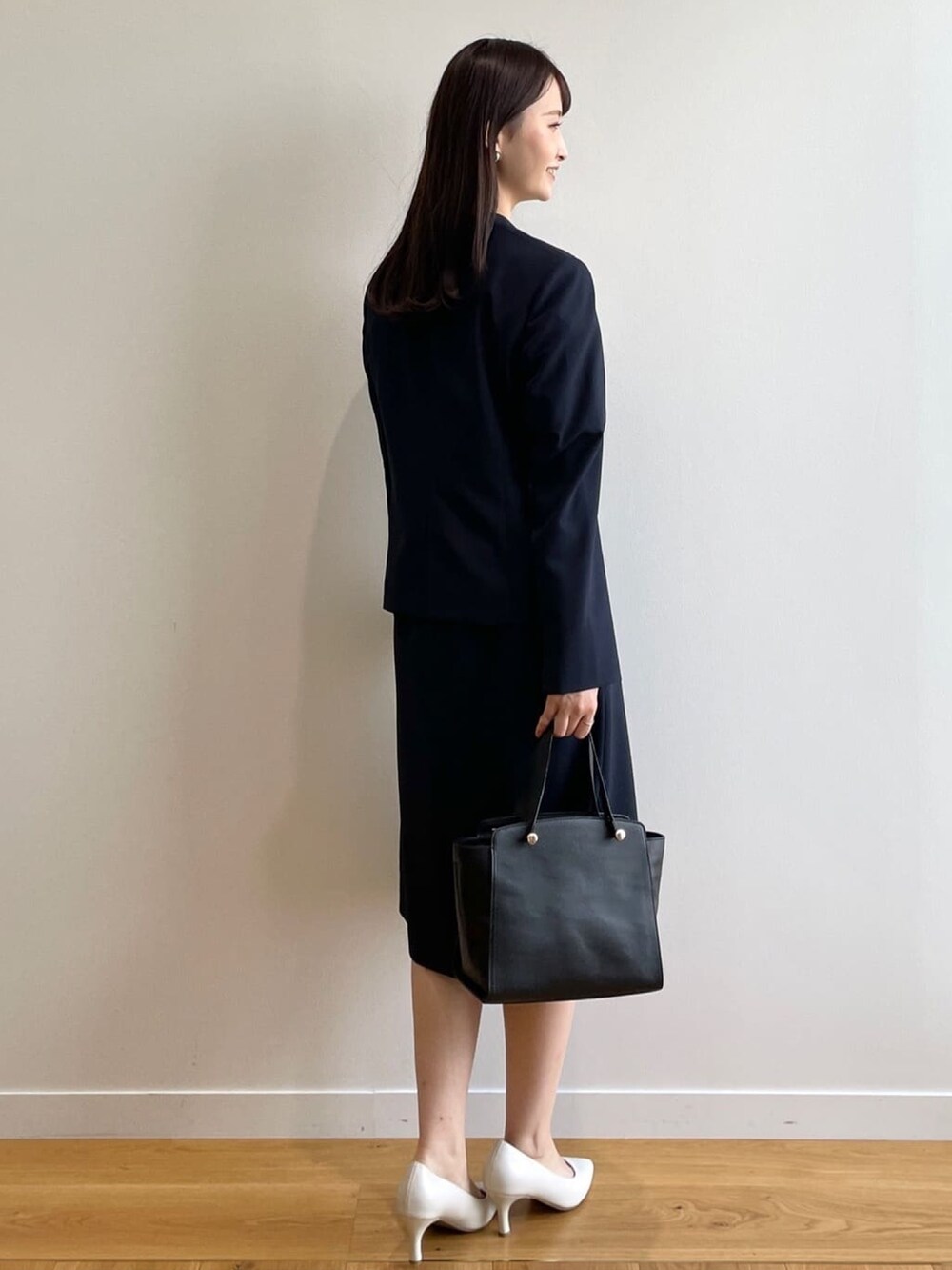 ブラック系のハンドバッグ、ホワイト系のパンプス、ブルー系のノーカラージャケットを着用したレディースの春コーディネートの3枚目の写真