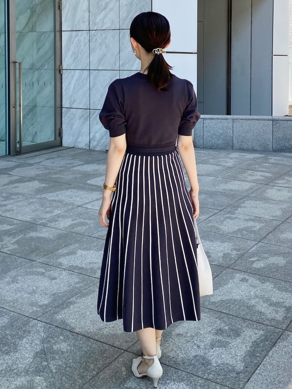 グレー系のワンピース、ホワイト系のパンプス、グレー系のトートバッグを着用したレディースの夏コーディネートの3枚目の写真