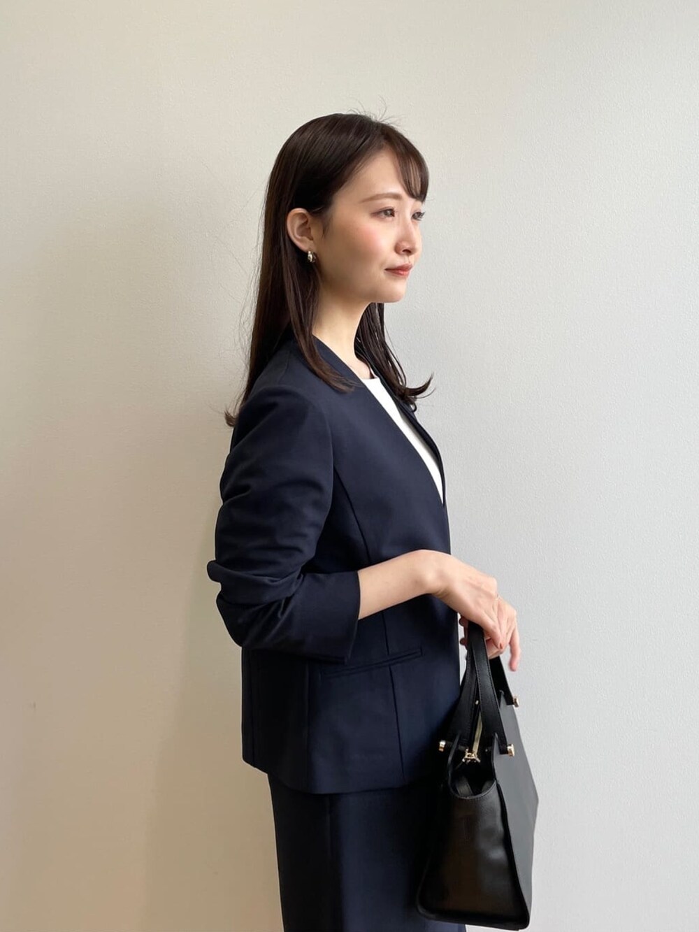 ブラック系のハンドバッグ、ホワイト系のパンプス、ブルー系のノーカラージャケットを着用したレディースの春コーディネートの6枚目の写真