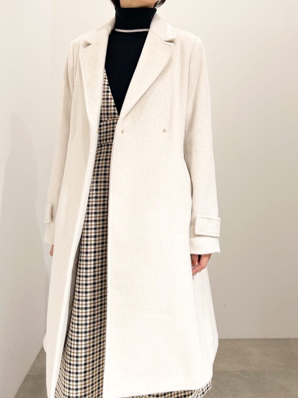 ベージュ系のチェスターコート、ブラック系のニット/セーター、ベージュ系のワンピースを着用したレディースの秋コーディネートの4枚目の写真